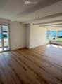 Empty room with wooden flooring, large windows, and a sliding glass door leading to a balcony.