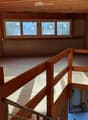 Empty wooden loft space with exposed beams, wooden floor, and large windows allowing natural light. No furniture or furnishings present.