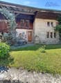 Two-story house with stone and wooden exterior, multiple windows, and a wooden front door. The house is surrounded by a well-maintained lawn and climbing plants.
