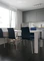 Modern kitchen with grey cabinets, white dining table, four black chairs, and various appliances including a microwave and a faucet.
