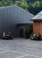 Modern building with grey and wooden facades, solar panels on the roof, outdoor seating area with picnic tables, and a barbecue area.