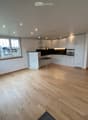 Empty room with light wooden flooring, white walls, and white cabinetry. Large windows provide natural light, and the space is unfurnished.