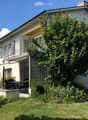 Two-story white house with a balcony, surrounded by a well-maintained garden and lawn.
