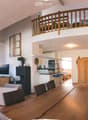 Open-plan living and dining area with a fireplace, television, sofa, coffee table, dining table with chairs, and a kitchen area with stools.