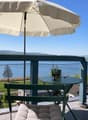 Balcony with a view of a lake and surrounding landscape, featuring a round table, chairs, and an umbrella.