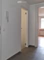 Empty hallway with tiled floor, white walls, and two doors leading to other rooms. One door has a visible telephone and light switch.
