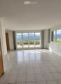 Empty hallway with tiled floor, white walls, large windows, and sliding glass doors leading to an outdoor area.