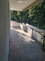 Balcony with tiled floor, modern railing, and a view of greenery and parked cars.