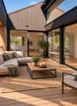 Modern outdoor balcony with wooden decking, a sectional sofa, coffee table, armchair, lantern, and potted plants.