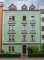 Three-story green house with white trim, multiple windows, decorative roofline, and a bicycle parked near the entrance.
