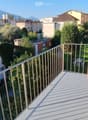 Balcony with metal railing, overlooking a residential area with houses, trees, and a clear blue sky.