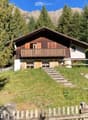 Two-story wooden house with a balcony, surrounded by trees and mountains.