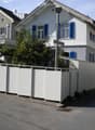 Two-story residential house with white walls, blue shutters, and a garage. A white fence surrounds the property, and a car is parked nearby.