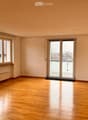Empty room with wooden flooring, large windows, and a sliding glass door leading to a balcony.