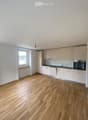 Empty kitchen with light wooden flooring, white cabinets, and a window letting in natural light. No appliances or furniture are present.