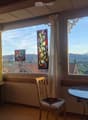 Bright room with large windows offering a scenic mountain view, featuring a wooden chair, a round glass table, and decorative curtains.