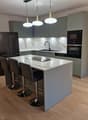 Modern kitchen with grey cabinets, marble countertops, stainless steel appliances, and pendant lights above the island.