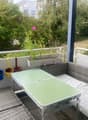 Balcony with a green table, wicker sofa, and hanging flower pots.