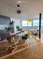 Open-plan living and dining area with modern furniture, including a dining table with chairs, a sofa, and a kitchen area with cabinets and appliances.