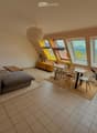 Bright living room with large windows offering a scenic mountain view, featuring a grey sectional sofa, coffee table, dining area with a table and chairs, and several potted plants.