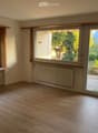 Empty room with wooden flooring, large windows, radiators, and sliding glass doors opening to a garden.