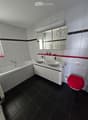 Modern bathroom with black tiled floor, white tiled walls, double sink vanity, bathtub, toilet with red seat cover, and a large mirror with decorative design.