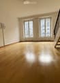 Empty room with wooden flooring, large windows, and a staircase leading upwards.