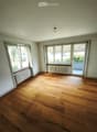 Empty room with wooden flooring, large windows, radiators, and a sliding glass door leading to a balcony.