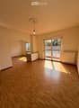 Empty room with wooden flooring, large sliding glass door leading to a balcony, and a small window on the left side.
