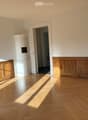 Empty room with wooden herringbone flooring, white walls, and a white cylindrical object in the center. Two doorways lead to adjacent spaces.