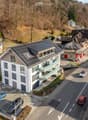 Aerial view of a residential area with multiple houses, solar panels on roofs, parked cars, and a road running through the neighborhood.