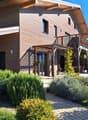 Two-story wooden house with a balcony, covered patio, and well-maintained garden with shrubs and a lawn.