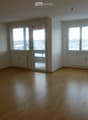 Empty room with wooden flooring, white walls, large windows, and a sliding glass door leading to a balcony.