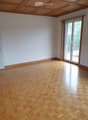 Empty room with wooden herringbone flooring, white walls, and large sliding glass doors leading to a balcony.