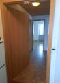 A narrow hallway with wooden doors, tiled floor, and a visible room at the end with a radiator and window.