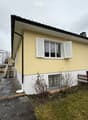 Raised ground floor, yellow and white painted house, white shutters, gravel pathway, fenced garden, chimney, metal railings on staircase