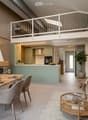Modern open-plan living and dining area with a sofa, coffee table, dining table, and kitchen island. Features a fireplace, pendant light, and decorative vases with plants.