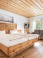 Cozy bedroom with wooden bed, nightstand, sofa, and TV, featuring large windows with a scenic view.