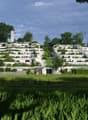 A large, modern residential complex with multiple white buildings arranged on a hillside, surrounded by lush greenery and trees.