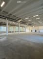 Large, empty industrial-style space with concrete floors, white walls, exposed ceiling beams, and large windows allowing natural light.