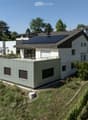 Modern two-story house with white walls, dark roof, solar panels, and a raised ground floor section with a green facade.
