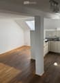 Bright, open loft-style room with wooden flooring, white walls, and a small kitchenette area featuring white cabinets and a sink.
