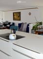 Open-plan living and dining area with a modern kitchen island, sofas, a piano, and large windows offering a scenic view.