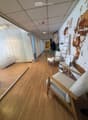 Modern hallway with wooden flooring, glass walls, and a seating area featuring a chair, small table, and plant.