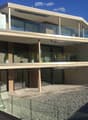 Modern two-story house with large glass balconies, beige and brown exterior, and a raised ground floor.