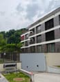 Modern multi-story residential building with balconies, large windows, and contemporary design, surrounded by greenery and a small garden area with a metal staircase.