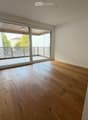 Empty room with light wooden flooring, white walls, and large sliding glass doors leading to a balcony.