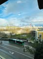 Balcony view overlooking a city street with a green and white bus, buildings, trees, and a clear sky.
