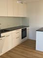 Modern kitchen with white cabinets, black countertops, a sink, and an oven. The floor is wooden.