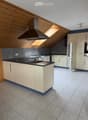 Modern kitchen with light wood cabinets, black countertops, a central island, and stainless steel appliances including a range hood, oven, and refrigerator. The space features a skylight and tiled flooring.
